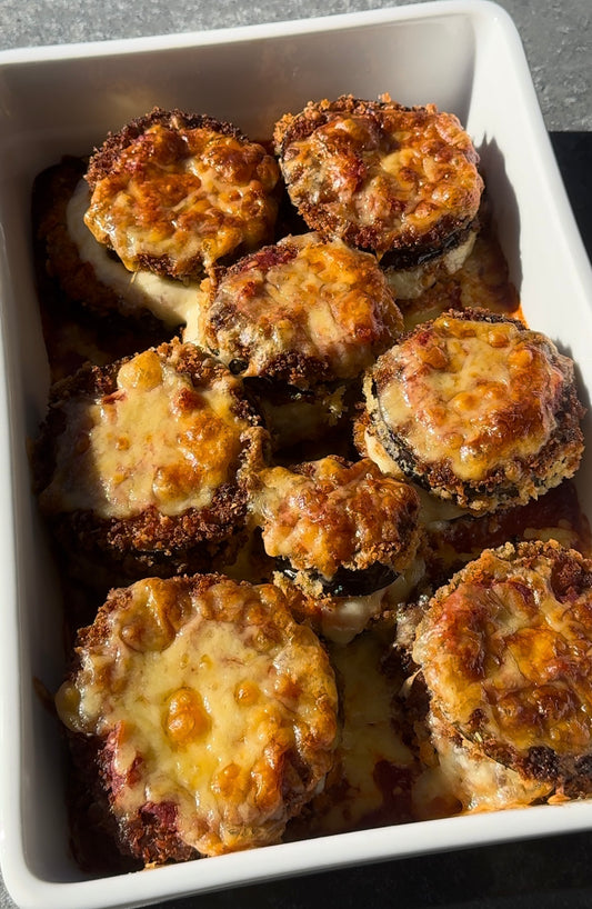 white tray filled with eight stacks of fried eggplant in marinara sauce, topped with crispy baked cheese.