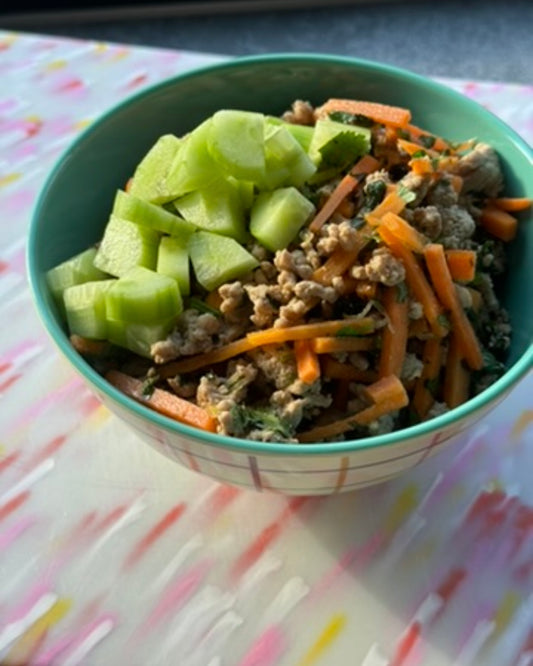 green bowl sitting on pink chopping board filled with rice and topped with a Thai spicy larb and diced cucumbers.
