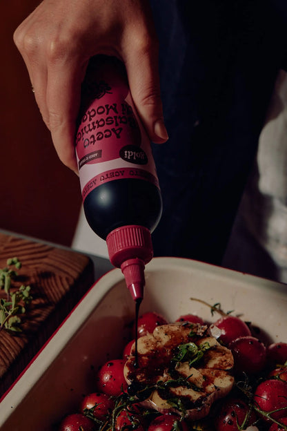 Balsamic vinegar being squeezed from bottle into a baking tray of vegetables.